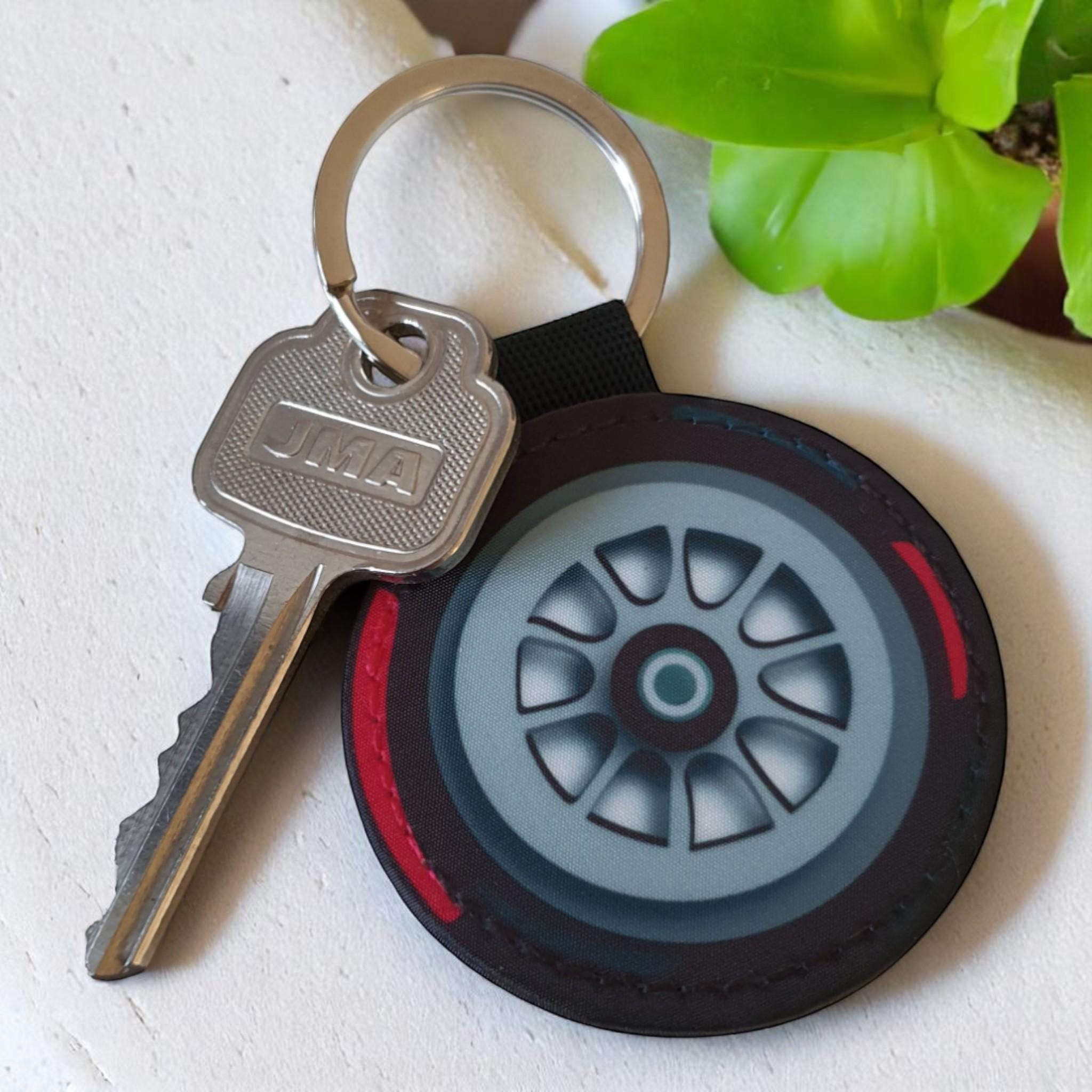 A black and red tire keychain with a silver rim and a silver key with the word 'JMA' on it.