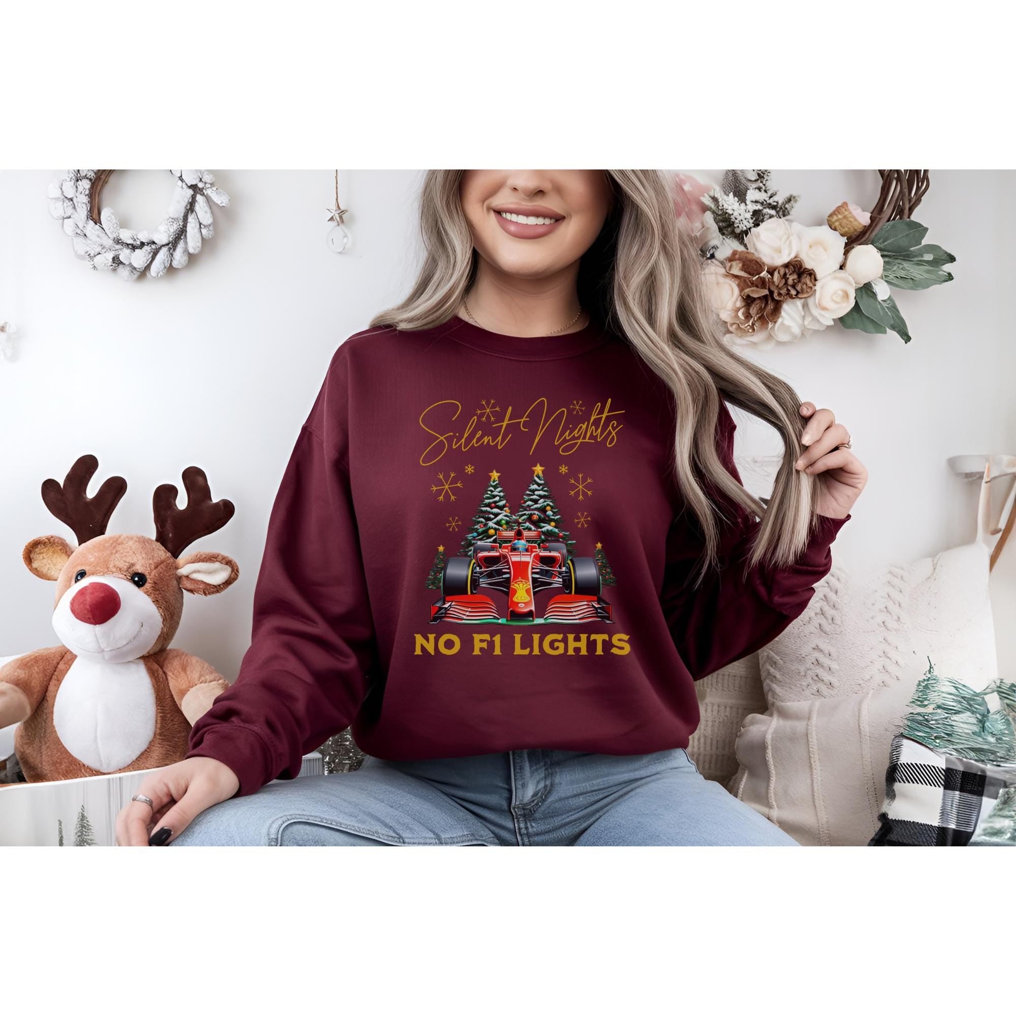Burgundy Christmas sweatshirt featuring a Formula 1 race car between two evergreen trees. The text on the sweatshirt says, &#39;Silent Nights, No F1 Lights.&#39;  The design includes snowflakes and is ideal for motorsports fans celebrating the holidays.