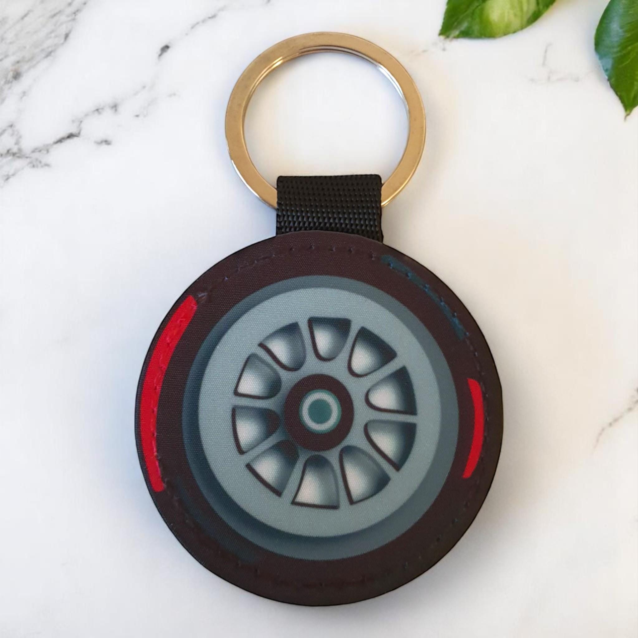 A black and red  f1 tire keychain with a silver rim and a black strap with a silver key ring.