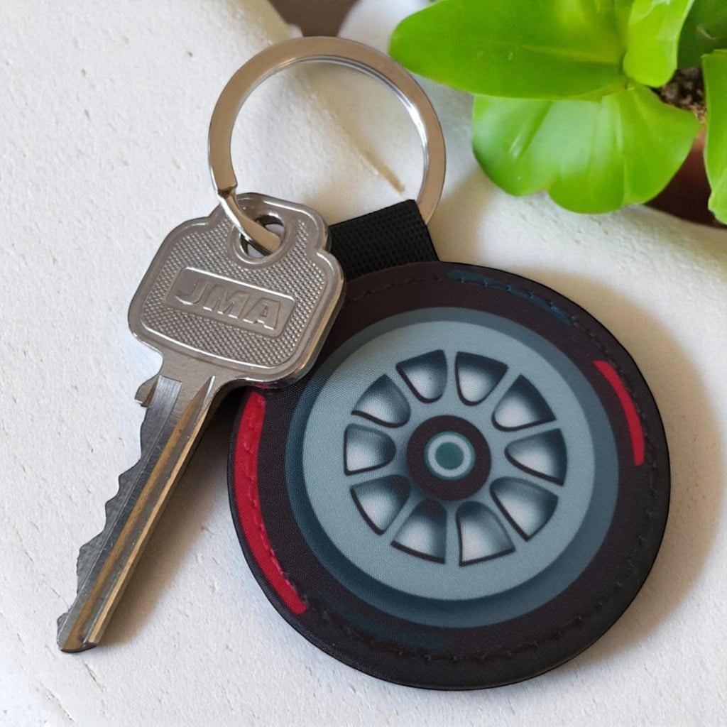 A black and red tire keychain with a silver rim and a silver key with the word &#39;JMA&#39; on it.