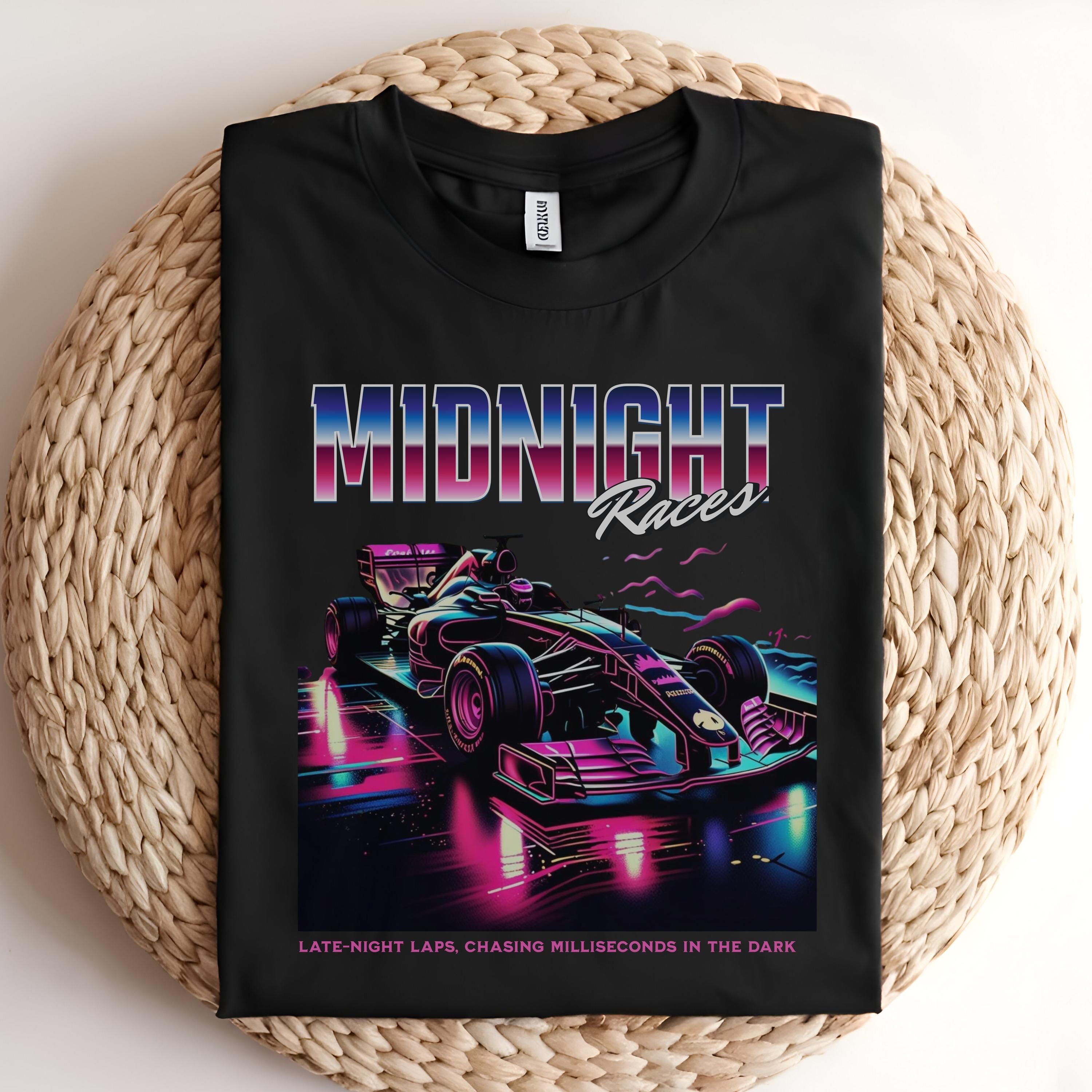 May include: A black t-shirt with a graphic of a purple and blue race car on a neon pink and blue track. The text &#39;MIDNIGHT Races&#39; is above the car in a pink, purple, and blue gradient. The text &#39;LATE-NIGHT LAPS, CHASING MILLISECONDS IN THE DARK&#39; is below the car in white text.