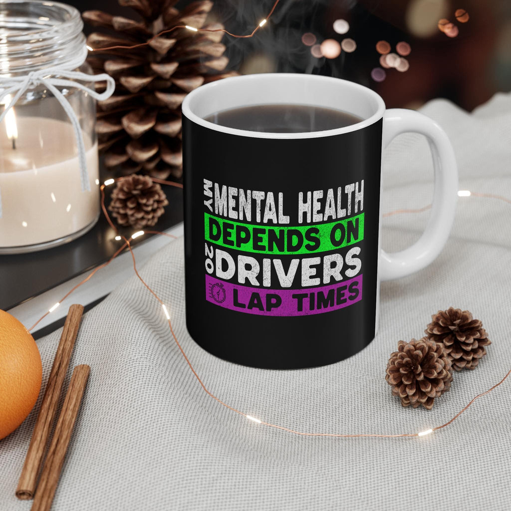 A black coffee mug with a white rim and handle. The mug has white text that reads &#39;My mental health depends on 20 drivers lap times&#39; in green and purple text.