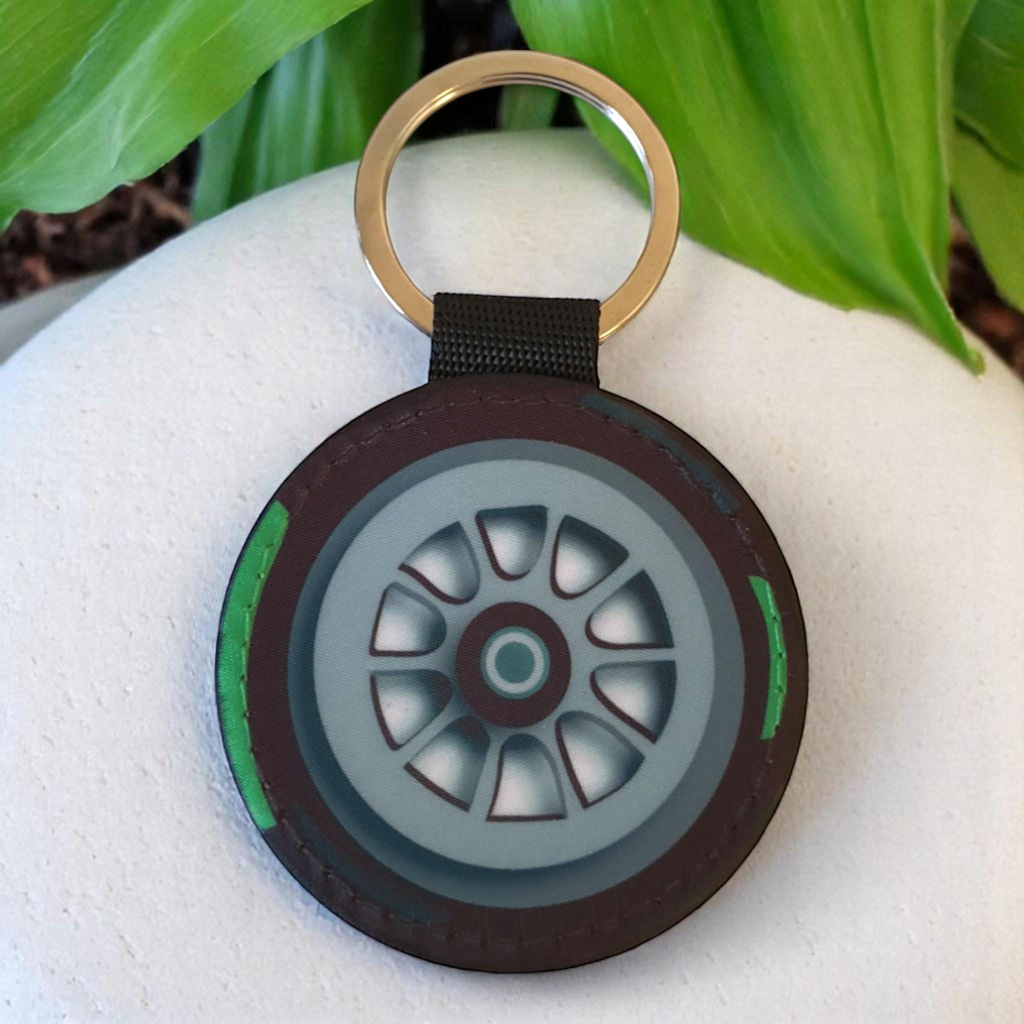 A black and green tire keychain with a silver rim and a black key ring.