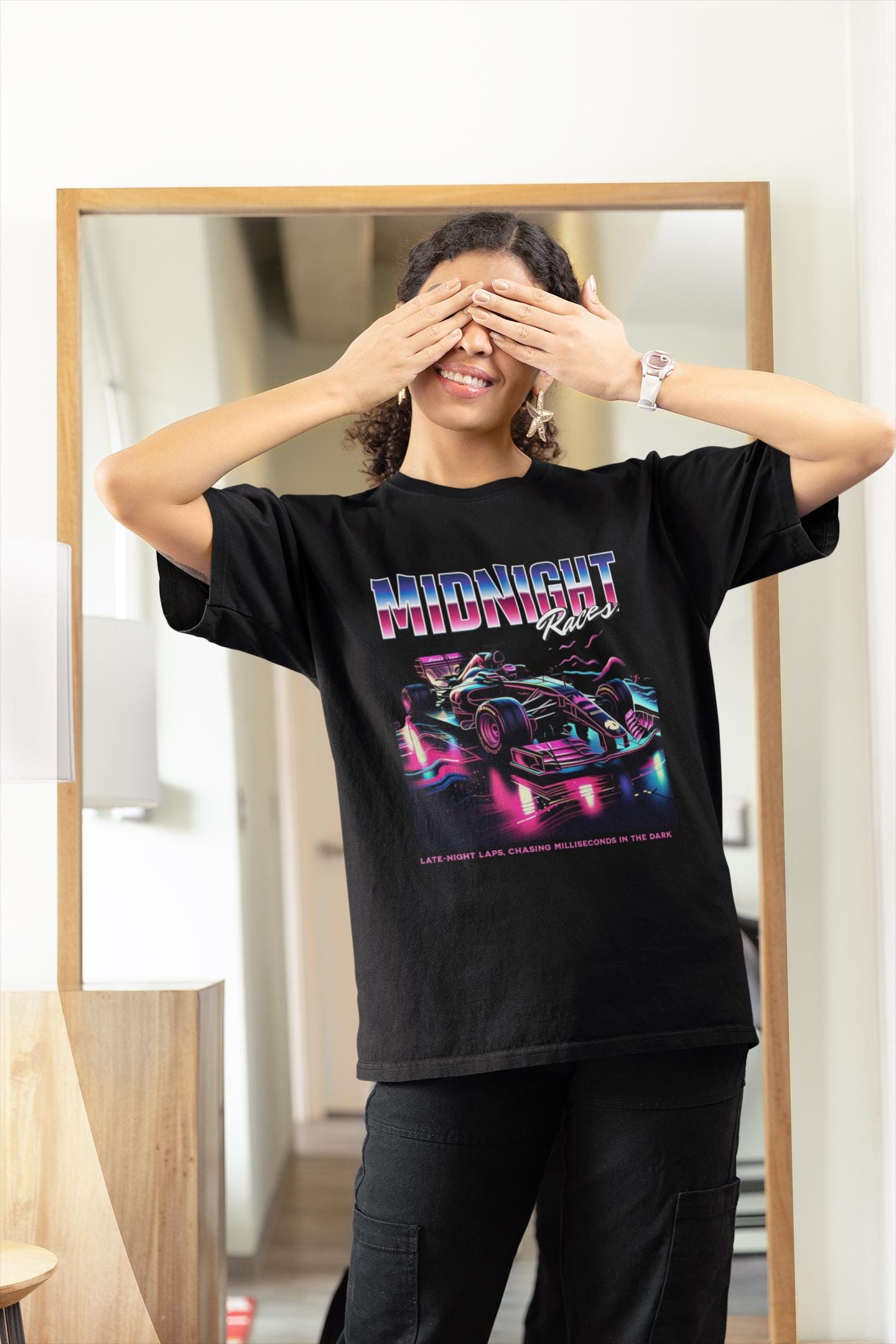 May include: A black t-shirt with a graphic of a race car in a neon pink, blue, and purple color scheme. The text &#39;MIDNIGHT Races&#39; is above the car and the text &#39;LATE-NIGHT LAPS. CHASING MILLISECONDS IN THE DARK.&#39; is below the car.