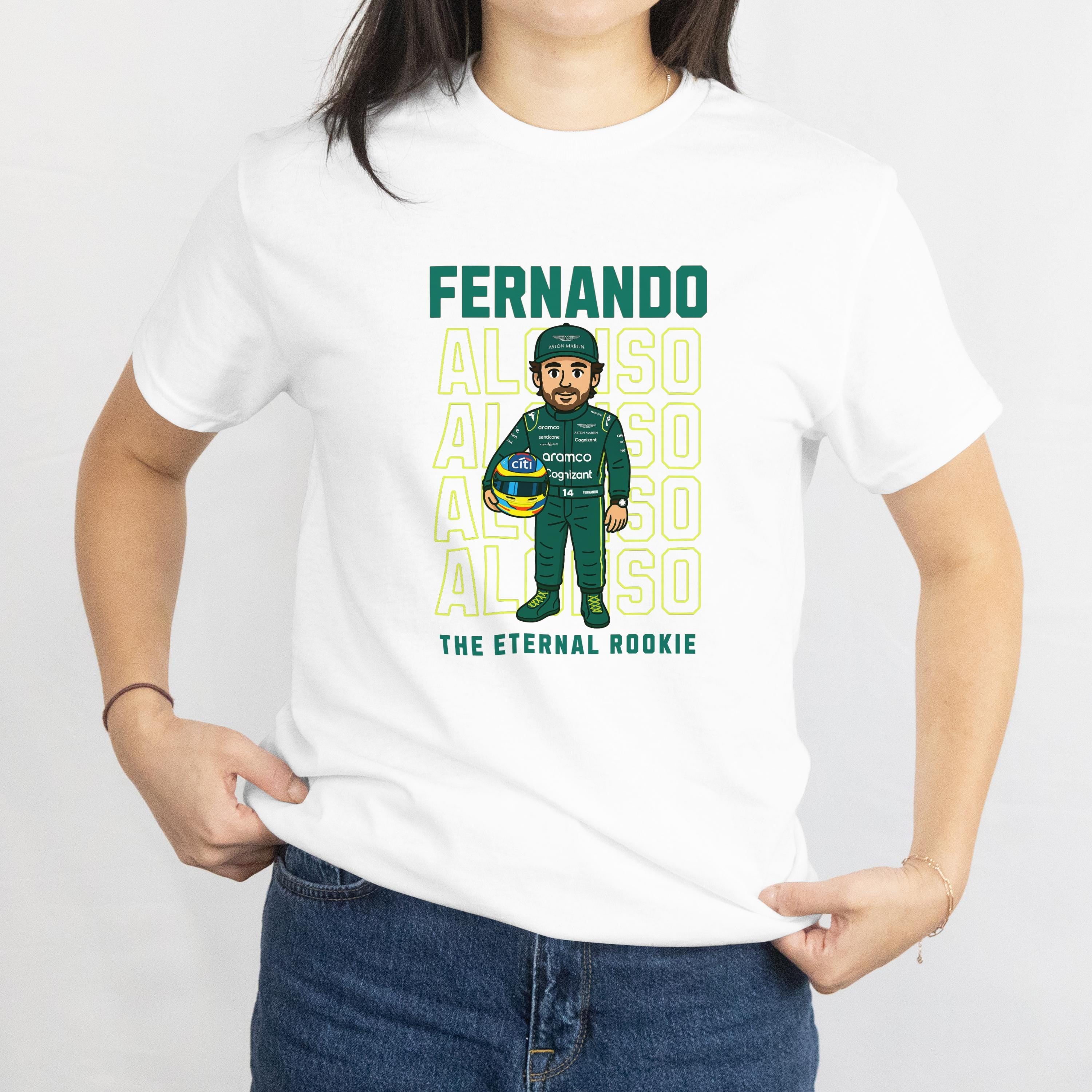 White t-shirt featuring a cartoon of a Formula 1 driver in a green racing suit and helmet, holding a helmet. The shirt has the name &#39;FERNANDO ALONSO&#39; in green block letters above the cartoon and the words &#39;THE ETERNAL ROOKIE&#39; below.