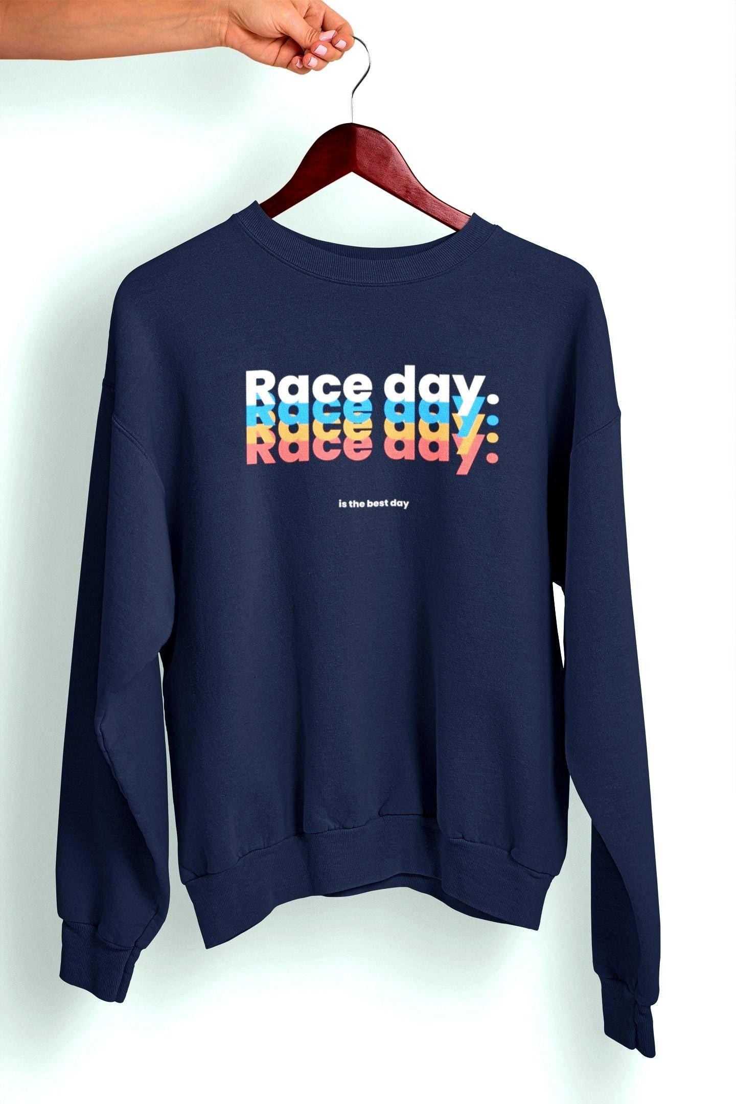 May include: A navy blue sweatshirt with the text &#39;Race day&#39; repeated three times in a stacked design. The text is in a retro font with each word in a different color: light blue, pink, and orange. Below the text is the phrase &#39;is the best day&#39; in a smaller font.
