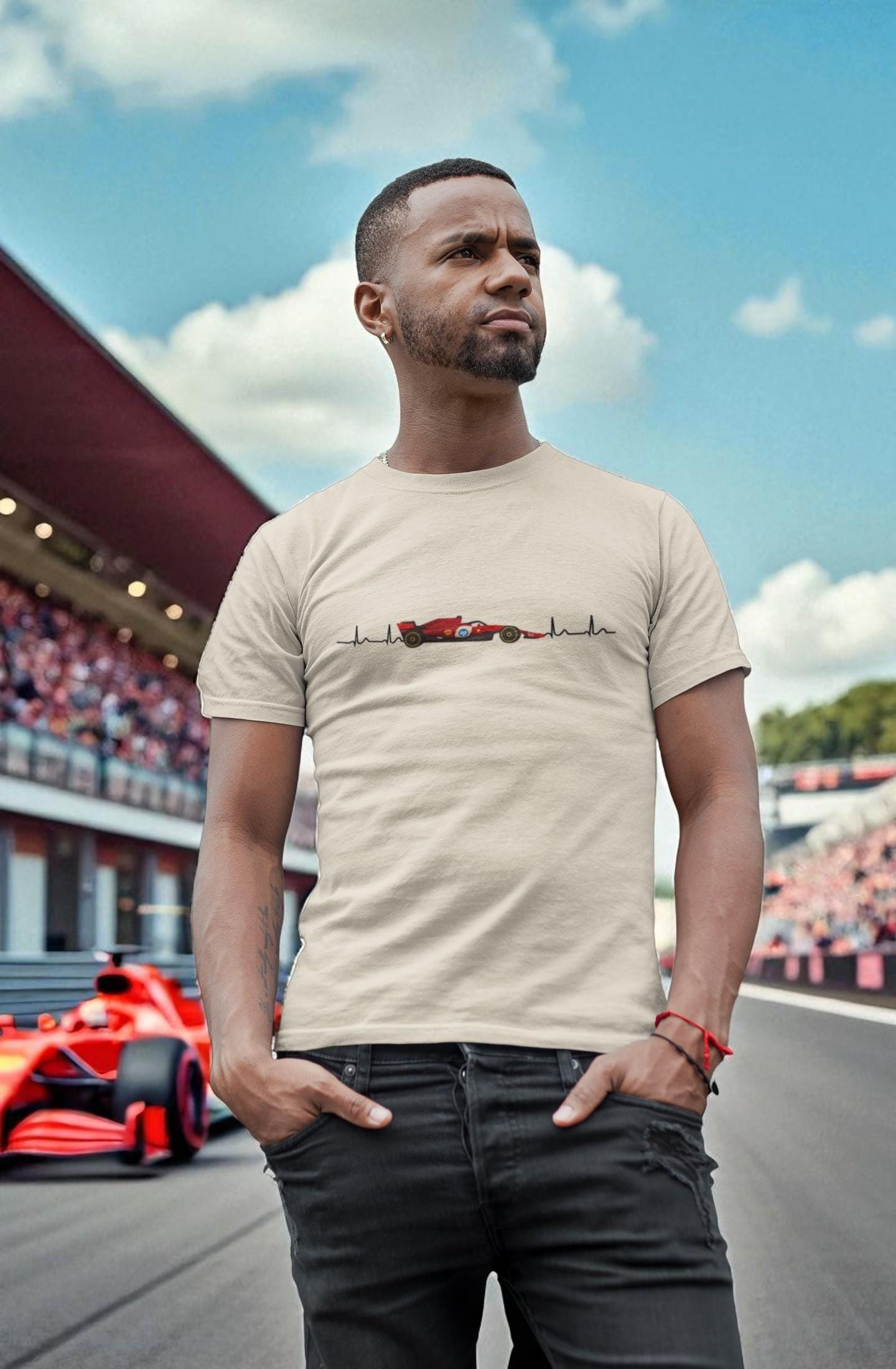 Man standing on a racetrack wearing a beige t-shirt with a red Ferrari  Formula 1 car and heartbeat line design, with a red race car and crowd in the background